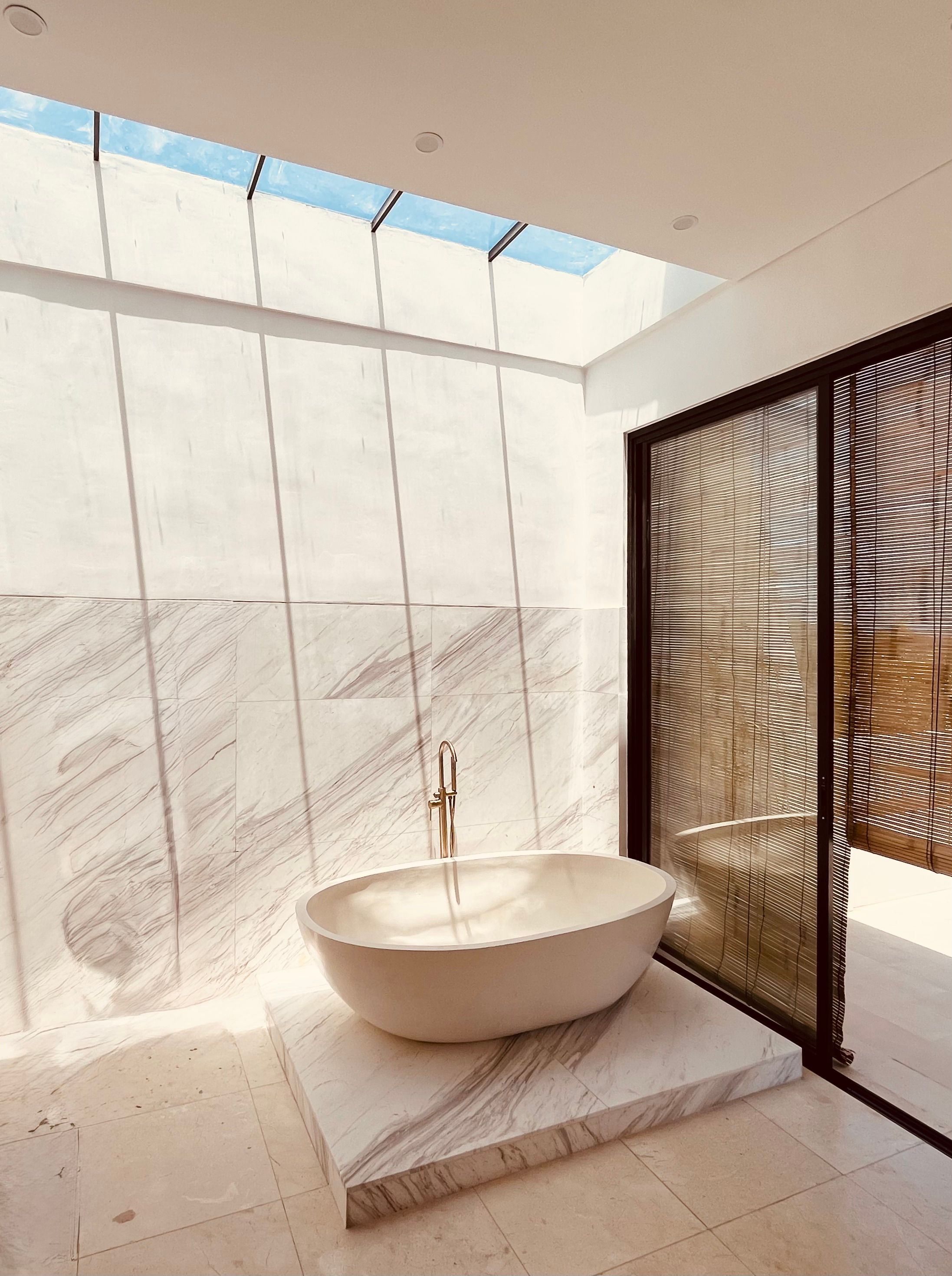 The master bathroom: a freestanding stone tub on a marble plinth under a long skylight open to the sky.