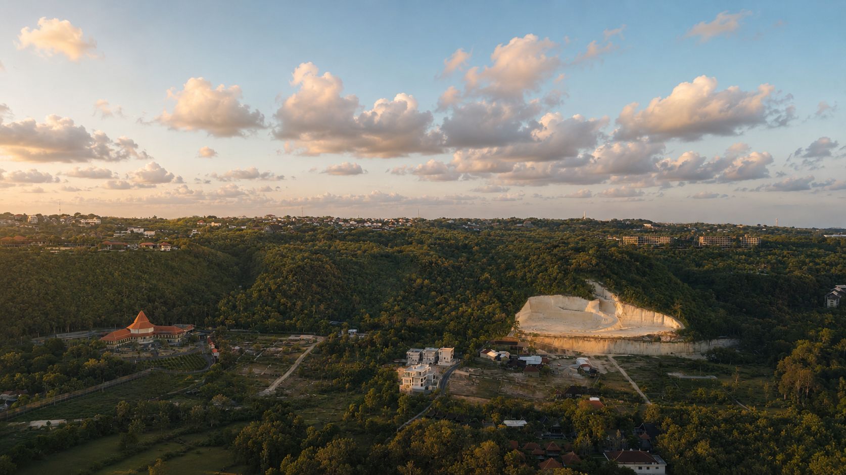 The villa high on the Bukit ridge at golden hour — white volumes among green hills, the resort and coast on the far horizon.