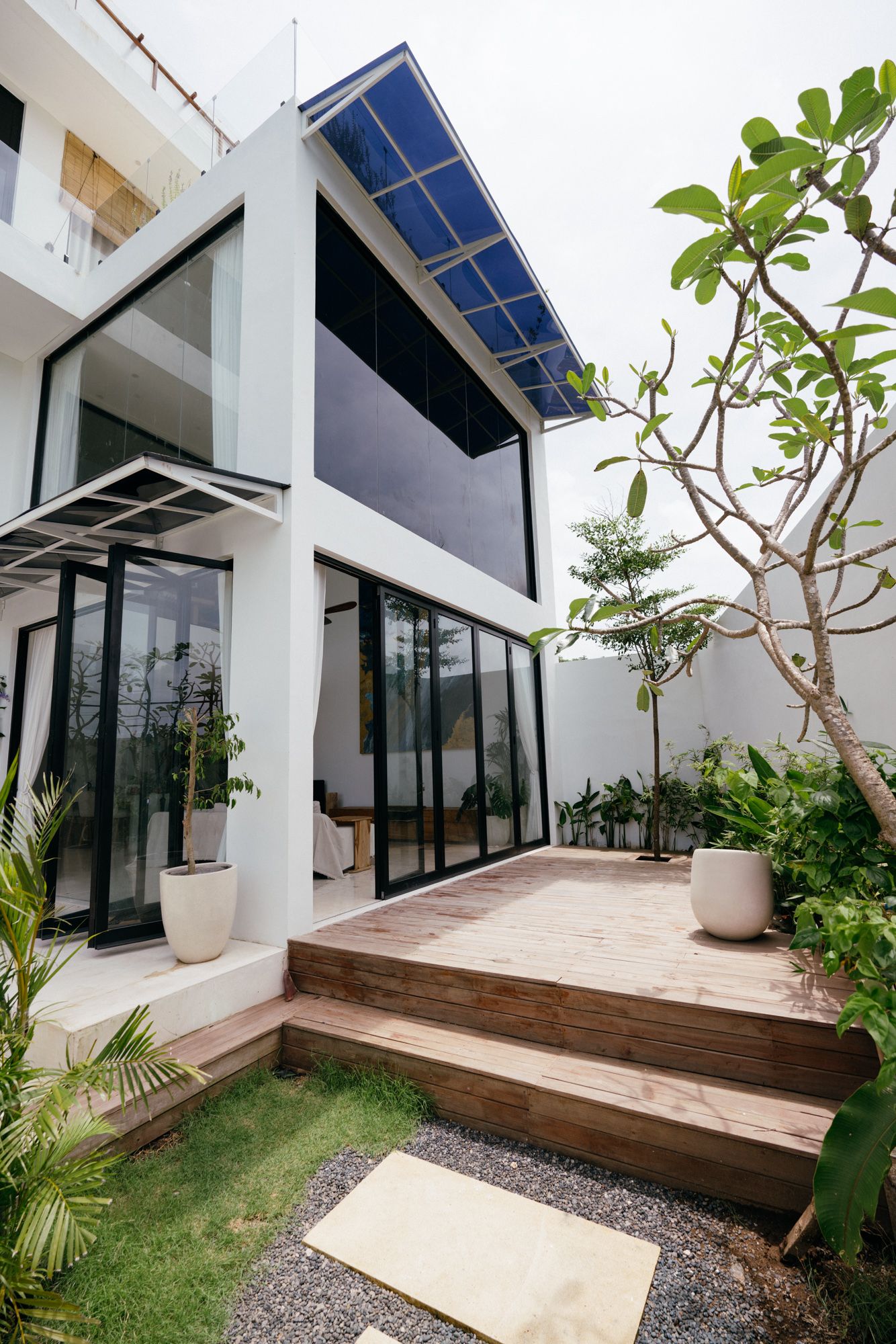 The timber deck terrace stepping down off the living room, potted frangipani at the corners.