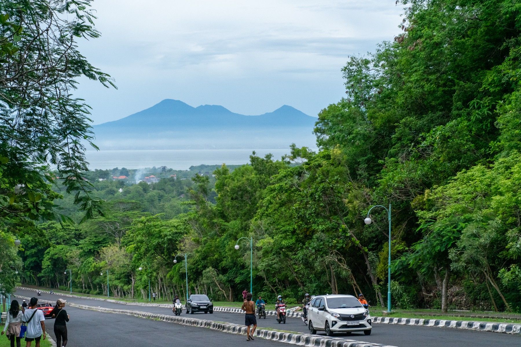The resort road dropping down the Bukit, the sea and the volcanoes across the bay beyond the trees.