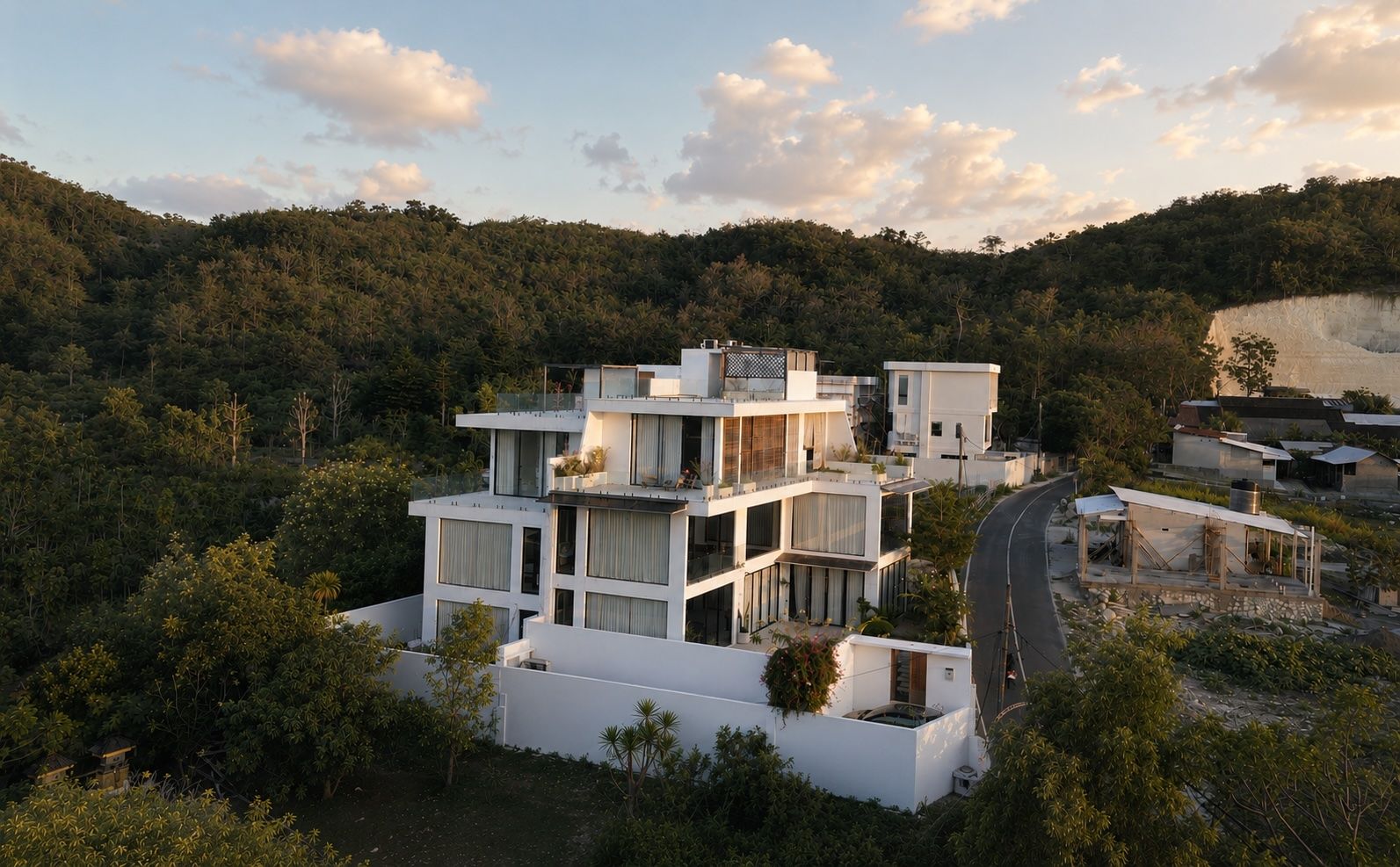 The white villa at The Summer Place in soft sunset light — stacked volumes on the Bukit ridge, the green hills beyond.