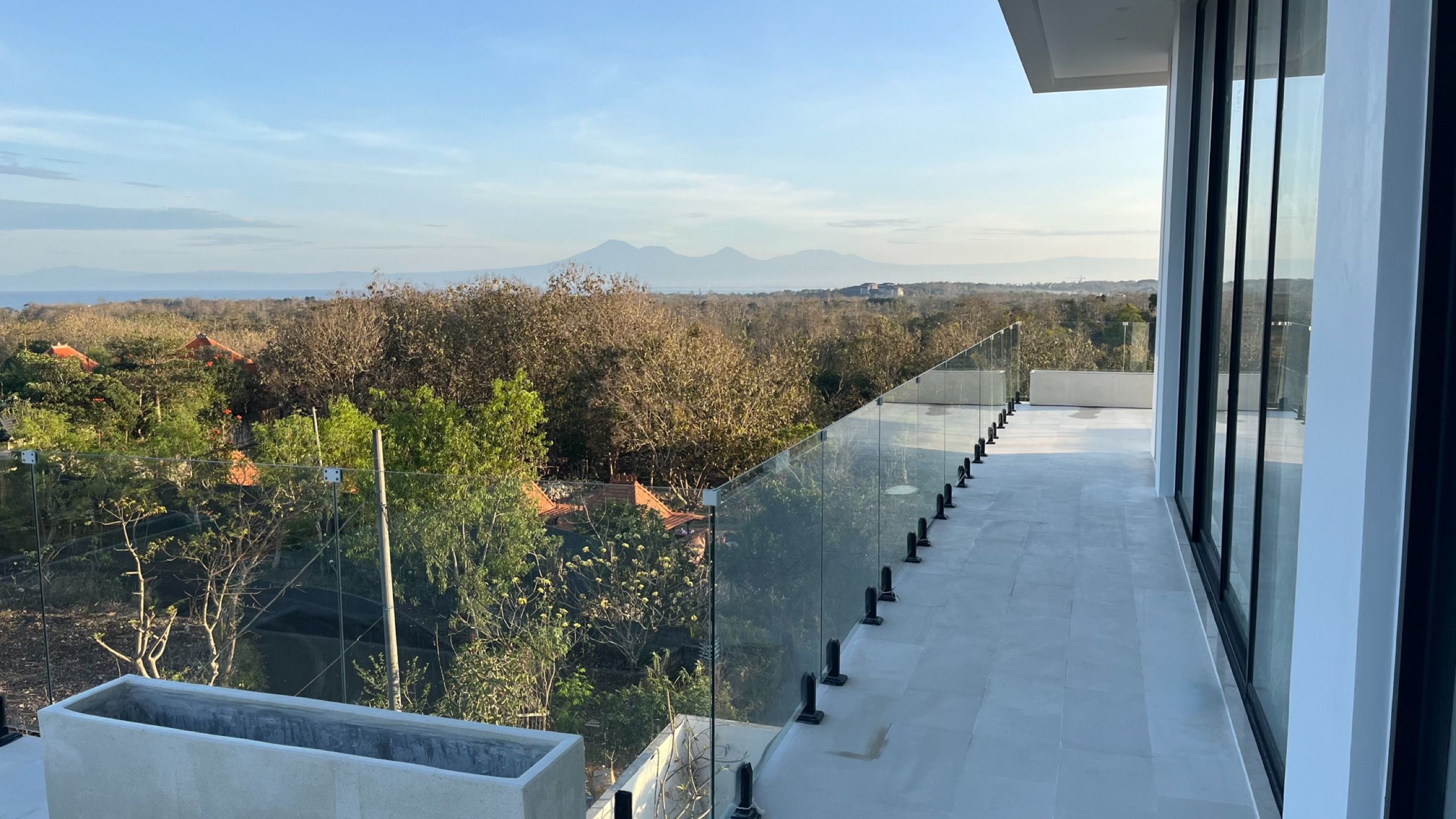 The master terrace behind a glass rail, the Bukit falling away to the distant sea and volcanoes.